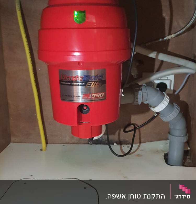 מכשיר טוחן אשפה אדום מתחת לכיור עם צינורות חיבור